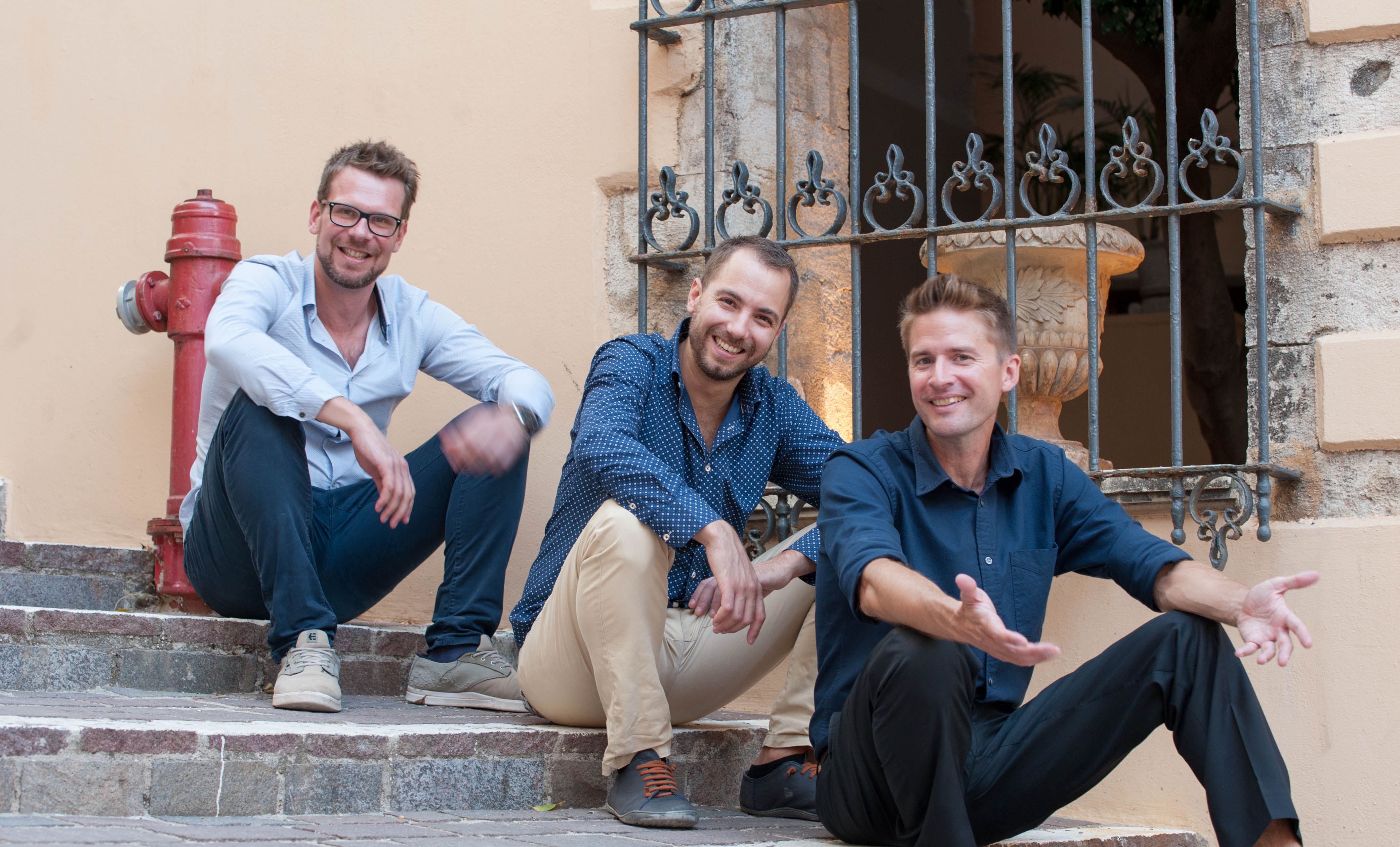 Color photo of Matthieu, Lefteris and Stefan seated on stairs beside red firepost.
